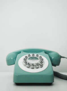 A close-up of a 1950s rotary dial telephone with a glossy pastel finish, resting on a lace doily.