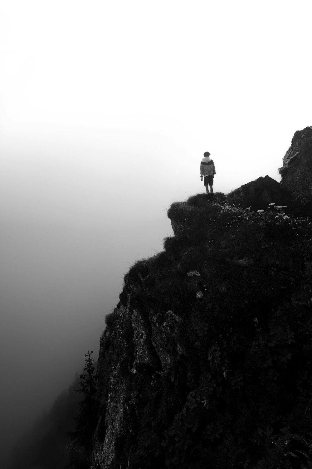 grayscale photography of person standing on cliff