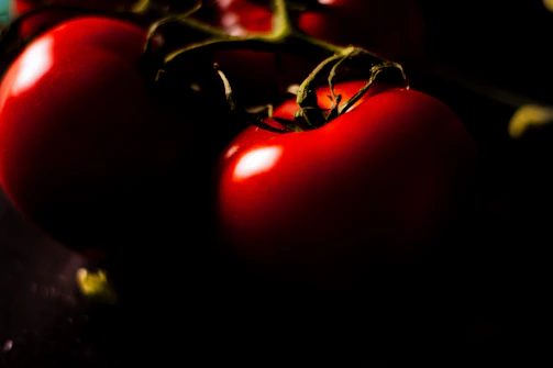 Close-up shot of ripe, deep crimson tomatoes on a rustic parchment background.