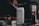 A can of Nütrl vodka soda with pineapple flavor is placed prominently in focus. It appears to have condensation, suggesting it is cold. In the background, there is a blurry image of someone grilling food, with a bottle containing sauce next to the can.