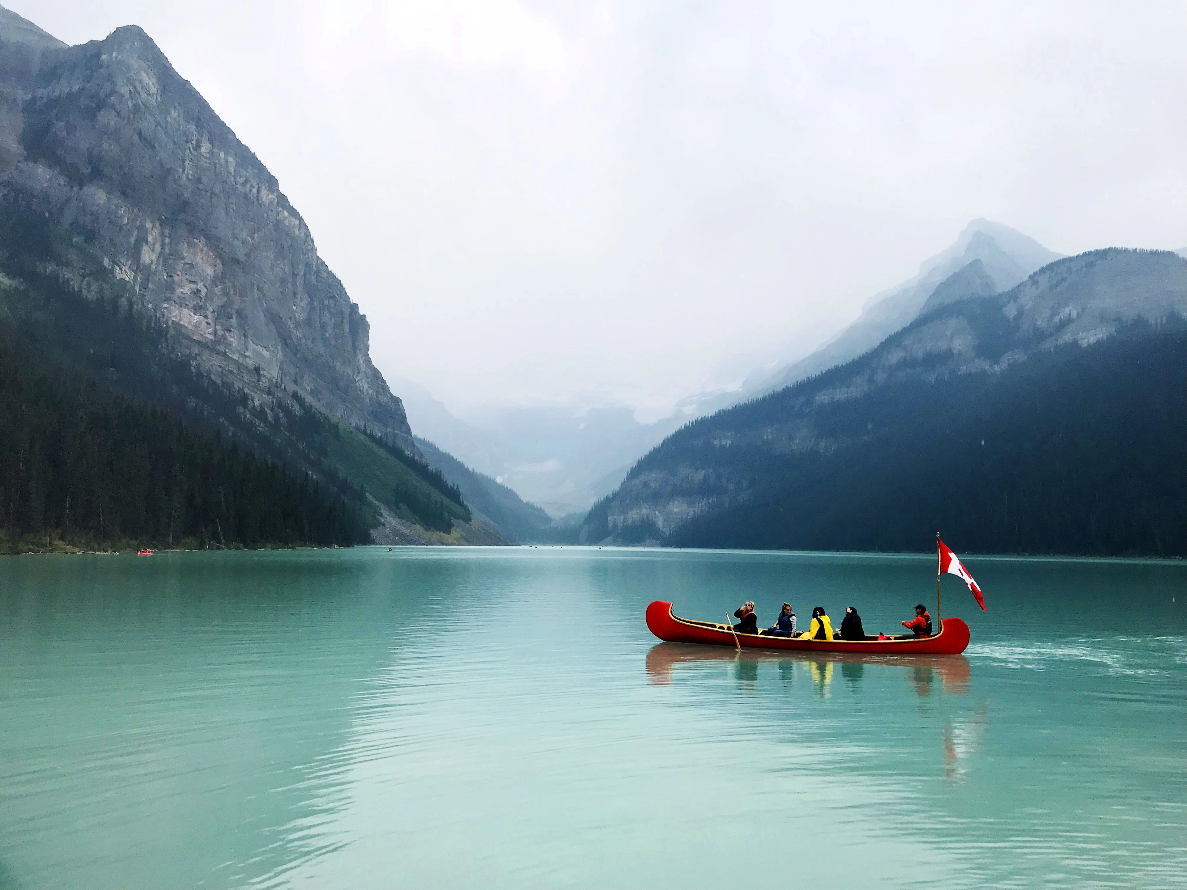 A red canoe on the calm turquoise water of Lake Louise, with light mist in the valley