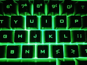 A close-up of a hand typing on a keyboard with neon green accents.