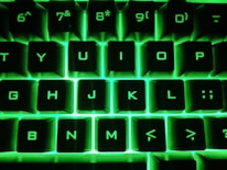 Close-up of hands typing on a keyboard with green backlit keys.