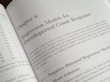 A textbook is open to Chapter 6, titled 'Regression Models for Overdispersed Count Response.' The page discusses various statistical models, including the negative binomial regression model, providing mathematical explanations and theoretical backgrounds.