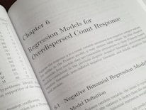 A textbook is open to Chapter 6, titled 'Regression Models for Overdispersed Count Response.' The page discusses various statistical models, including the negative binomial regression model, providing mathematical explanations and theoretical backgrounds.