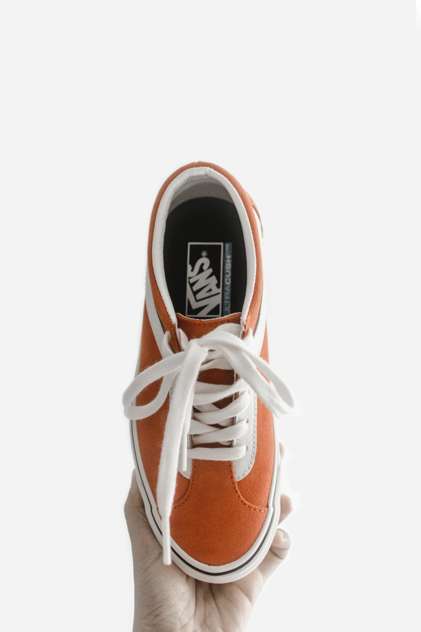 Orange canvas Vans low-top sneaker held against a white background