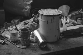 Workspace showing paint cans, brushes, and partially painted furniture resting on coverings.