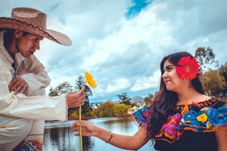 man giving woman yellow flower beside body of water