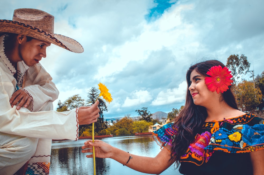 man giving woman yellow flower beside body of water