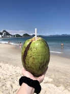 A hand holding a small coconut water bottle against a sunny beach background.