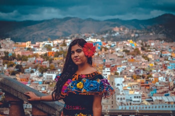 woman with red floral headdress taking photo with city background