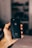 A hand holding a black smartphone with an Apple logo, set against a softly blurred background. The phone is an iPhone model.