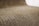 A close-up view of corrugated cardboard with a focus on its ridged texture. The light brown material creates a visually interesting pattern with its repetitive and undulating structure.