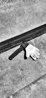 A single glove lies on a concrete surface near a step. The glove appears to be a sports glove, possibly for goalkeeping. The black and white color of the image creates a gritty, somber atmosphere.