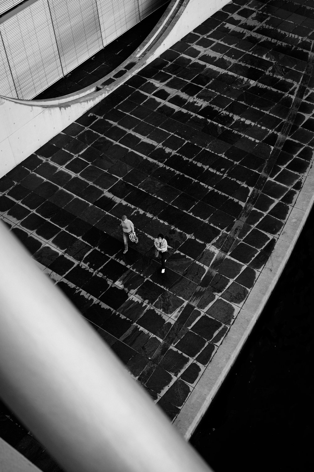 grayscale photography of two persons walking beside building