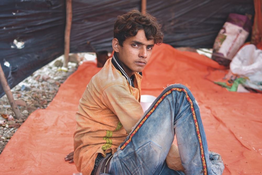 homem vestindo jeans azul sentado no tecido laranja