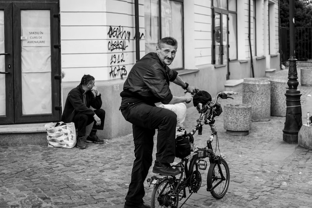 greyscale photography of man standing beside bicyce