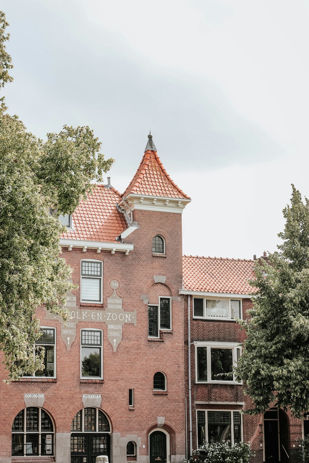 red brick building standing near trees under cloudy sky