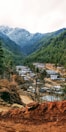 A mountainous landscape with dense green forests covering the slopes and peaks dusted with snow. A small village with wooden houses and tin roofs is nestled in the valley, surrounded by earthy paths and sparse trees.