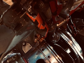 A close-up view of intricate mechanical gears and metal components, featuring detailed textures and reflections. The metal has a mixture of shiny and matte finishes, with visible bolts and labels.