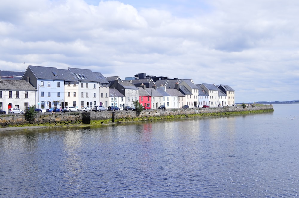 different vehicles near road beside houses viewing blue sea under white and blue skies