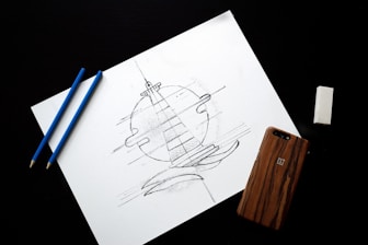 two blue coloring pencils near iPhone and lighthouse drawing