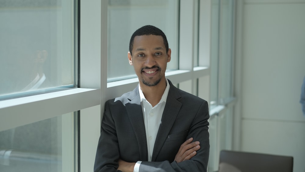 man wearing gray formal suit smiling while standing near glass window