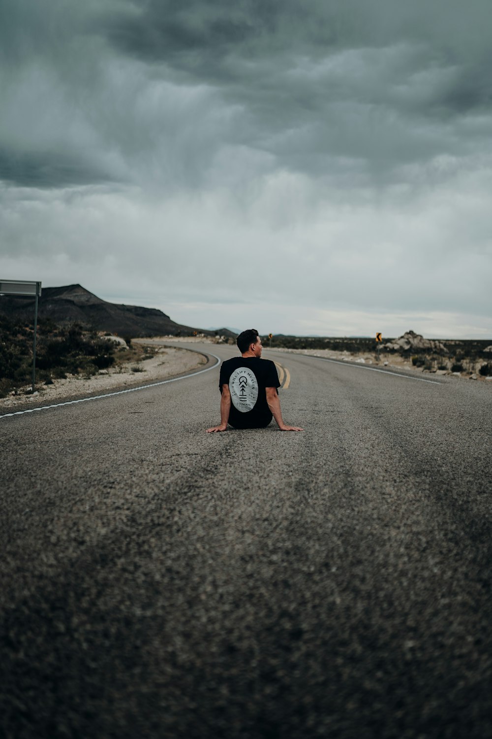 man sitting on road under grey sky