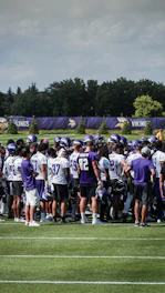 A team of football players wearing matching jerseys in a huddle on the field.