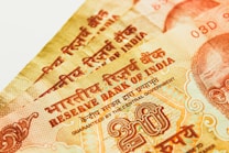 Multiple Indian currency notes close-up with intricate designs and text. The text includes Hindi and English, and there are visible numerals and symbols related to the Reserve Bank of India.