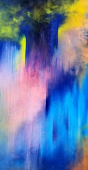 A vibrant abstract painting featuring a blend of colors including deep blue, purple, pink, yellow, and hints of green. The colors appear to merge and bleed into each other, creating a fluid, dreamlike effect. The top section of the image is darker, with intense cloud-like formations, while the bottom half transitions into lighter, more pastel shades.