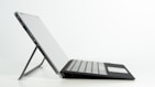 An ecostand folded flat next to a laptop, showcasing its portability and compact design.