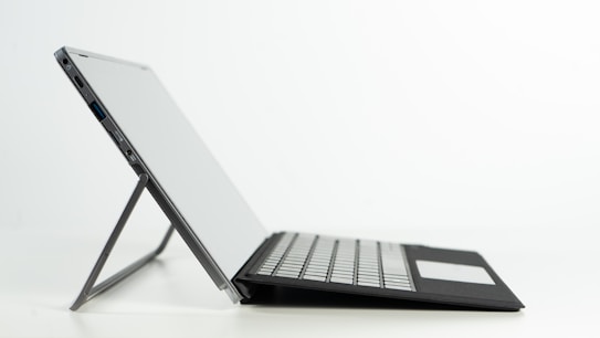 A side view of a sleek laptop with a detachable keyboard and a built-in stand. The laptop is positioned against a plain white background, showcasing its modern design and thin profile.