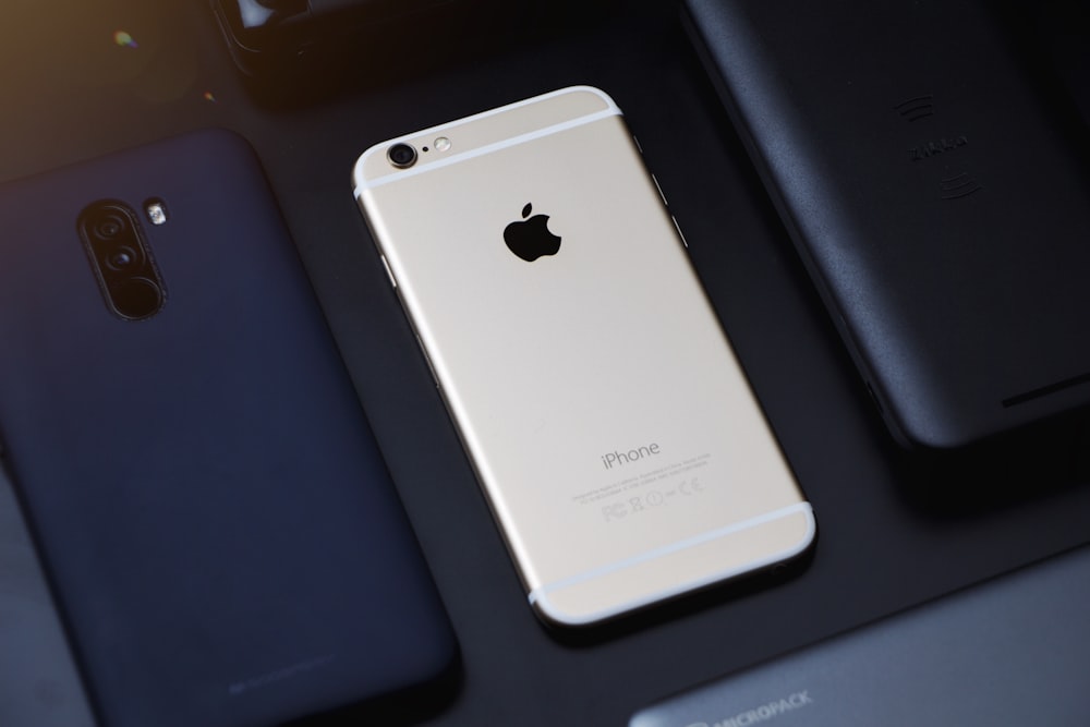 gold iPhone 6 beside black smartphone on black table