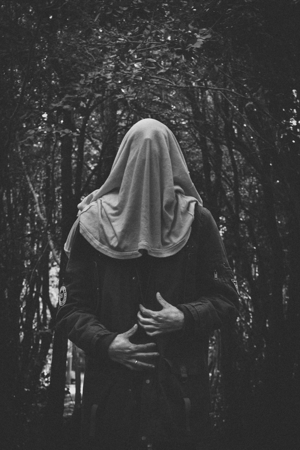 grayscale photo of man covering his face under tree