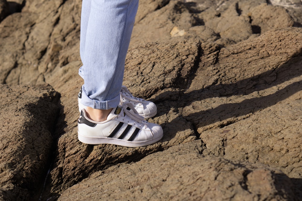 Foto Persona de pie sobre una roca con zapatillas adidas blancas y negras –  Imagen Gris gratis en Unsplash