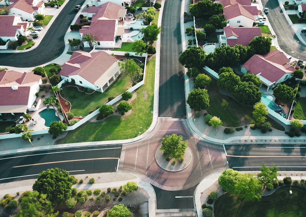 Aerial photo of a well-kept neighborhood, roundabout intersection joining blacktop streets, landscaped lawns, and uniform homes with reddish roofs in a hot real estate housing market in 2023.