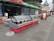 An outdoor food display featuring two large, red, refrigerated display cases filled with various dishes and beverages. These display cases are situated on a tiled walkway in front of a cafe or restaurant. The cafe has a canopy with green awnings and is part of a larger architectural environment with castle-like buildings in the background. There are some people walking in the distance and a few tables and chairs to the side of the display cases.