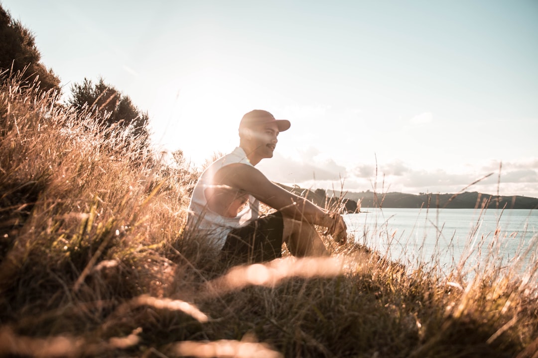 man wearing white sleeveless shirt sitting besides body of water