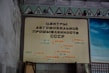 A wall displays a vintage sign written in Russian, featuring the words related to automotive industry centers in the USSR. The sign includes the names of various cities and automobile manufacturers. Above the sign, there are red-bordered triangular warning signs with various symbols.