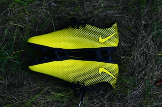 Two bright yellow and black soccer cleats with a textured pattern, placed against a backdrop of grass.