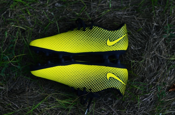 Two bright yellow and black soccer cleats with a textured pattern, placed against a backdrop of grass.