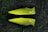 Two bright yellow and black soccer cleats with a textured pattern, placed against a backdrop of grass.