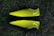 Two bright yellow and black soccer cleats with a textured pattern, placed against a backdrop of grass.