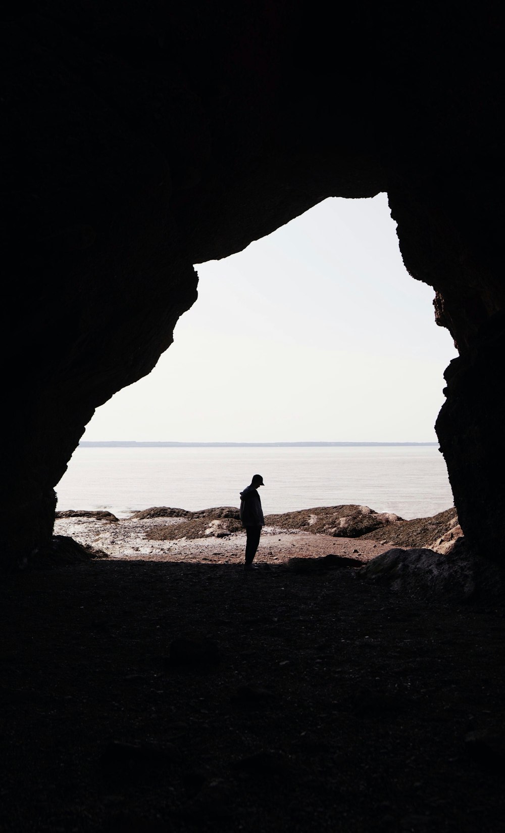 silhouette of person standing on cave entrance across horizon