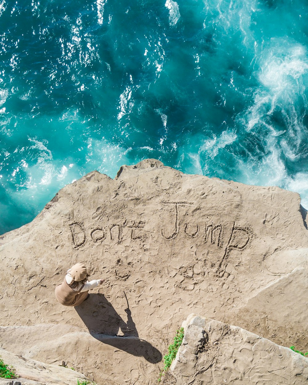person standing on cliff writing don't jump on ground