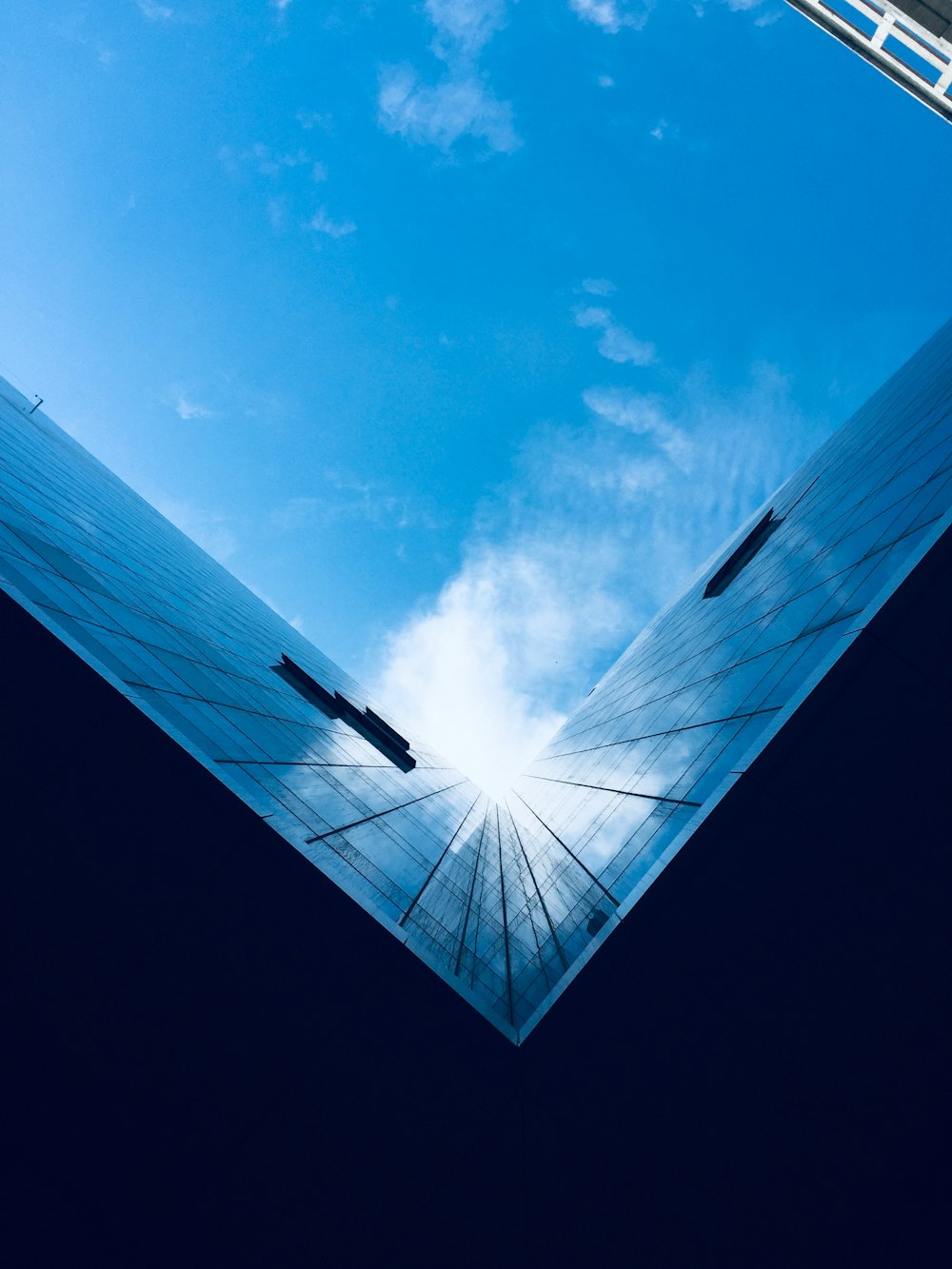 low-angle photography of blue glass walled high-rise building under blue and white skies