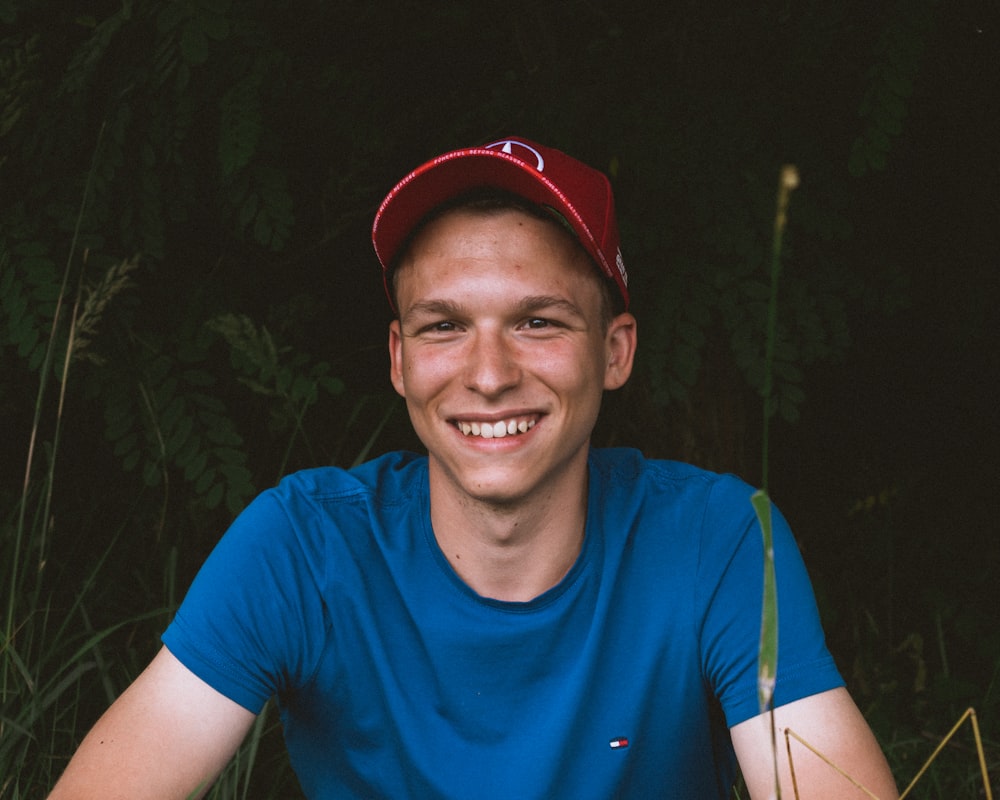 man in blue crew-neck shirt wearing red baseball cap near bushes