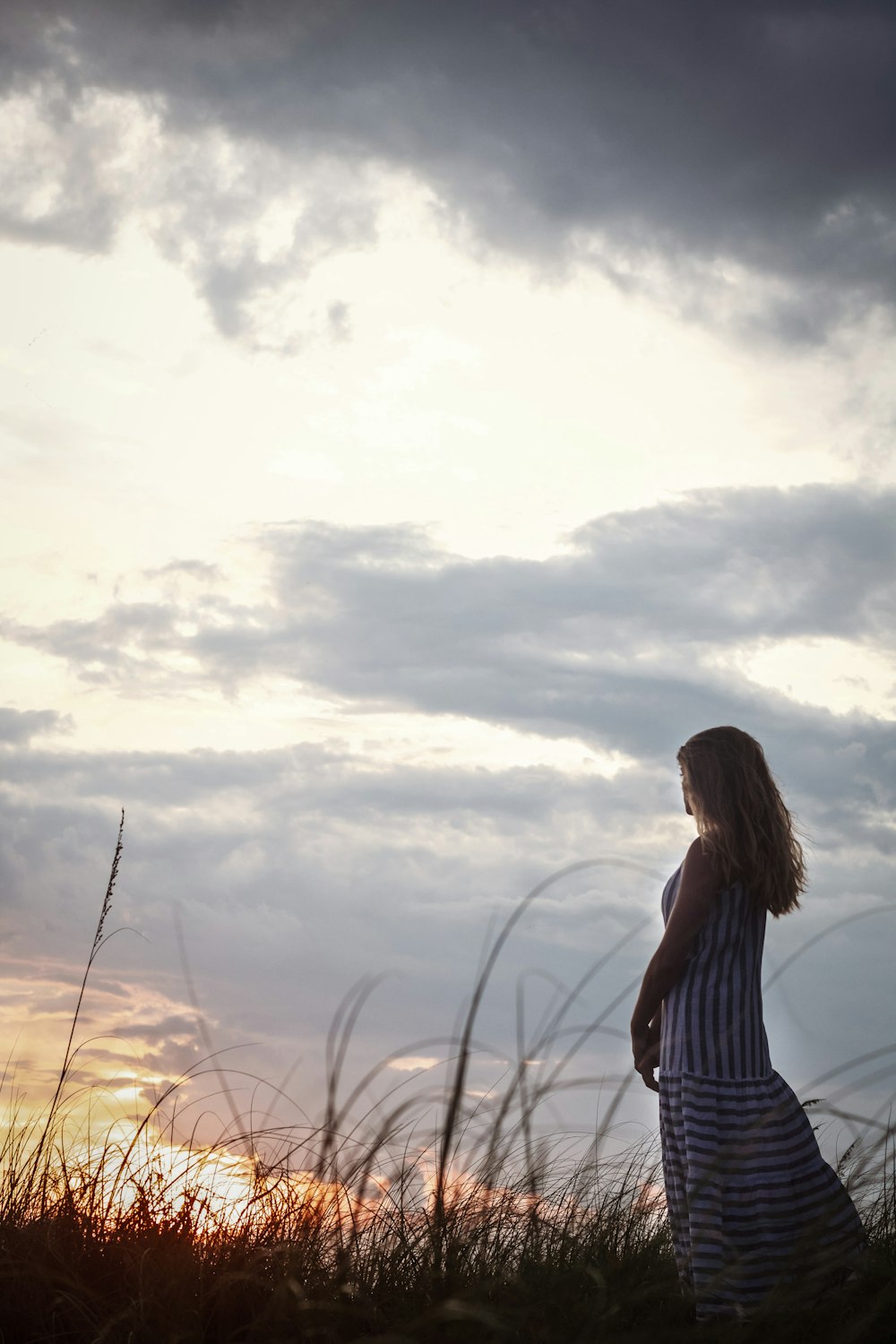 a woman standing in a field at sunset