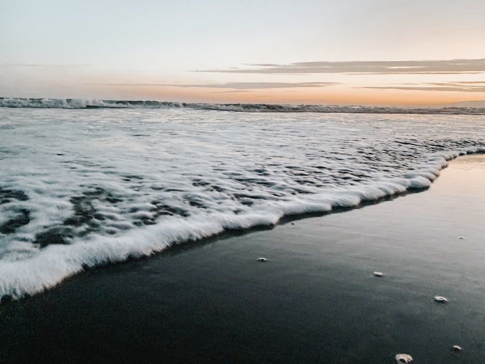 white sea foam on shore during sunset